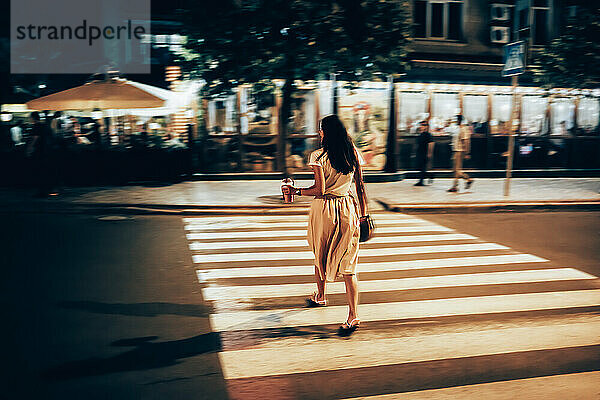 Frau mit Smoothie überquert nachts die Straße