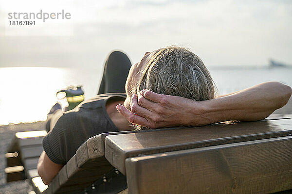 Reife Frau entspannt sich an einem sonnigen Tag auf einer Holzbank