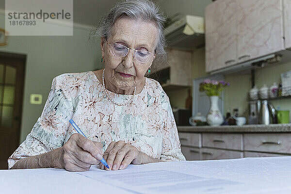 Ältere Frau mit Brille unterschreibt Hausversicherungspapiere auf dem Tisch
