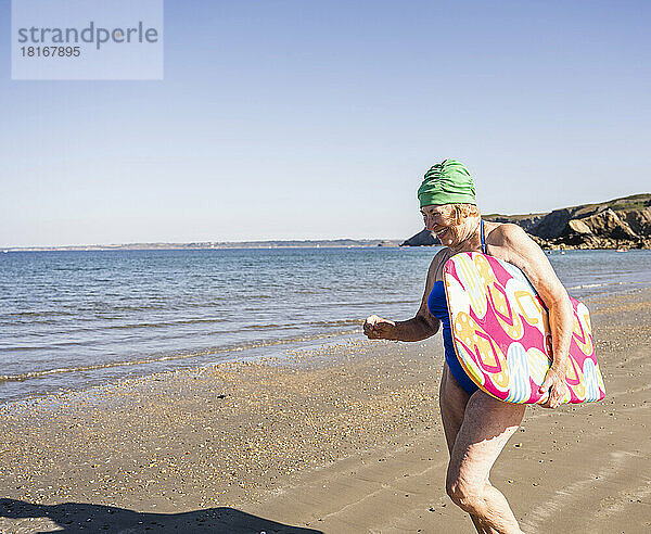 Ältere Frau mit Surfbrett  die Spaß am Strand hat