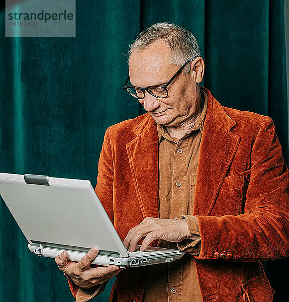 Älterer Mann benutzt Laptop vor Vorhang