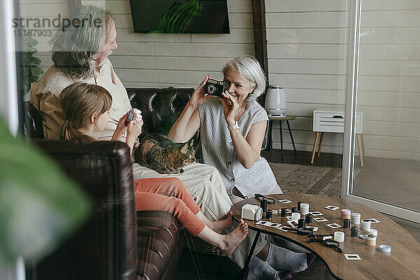 Frau fotografiert älteren Mann und Enkelin zu Hause mit einer Vintage-Filmkamera