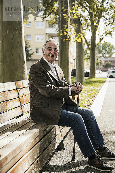 Happy senior man with walking cane sitting on bench