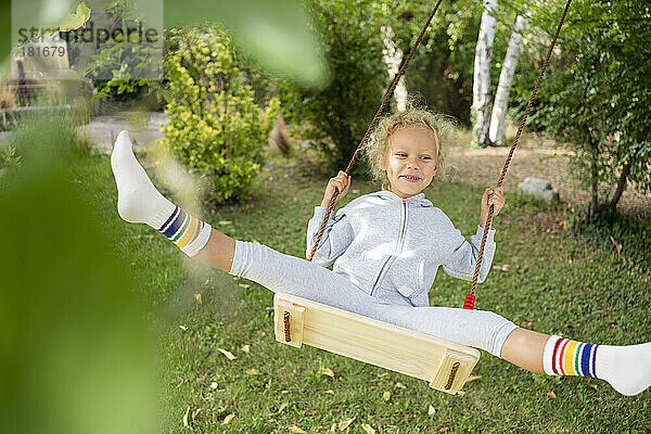 Fröhliches Mädchen schwingt auf der Schaukel im Garten