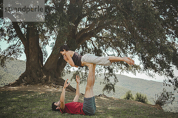 Junges Paar praktiziert Acroyoga unter einer Eiche