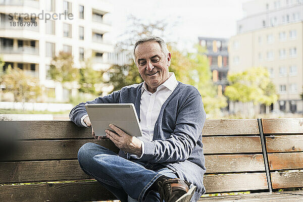 Lächelnder älterer Mann mit Tablet-PC auf Bank sitzend