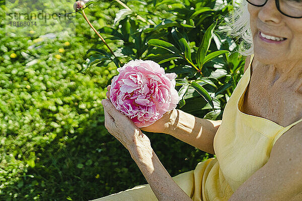 Frau hält an einem sonnigen Tag frische rosa Blumen im Garten