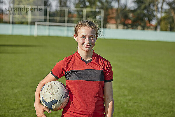 Smiling girl standing with soccer ball on sunny day