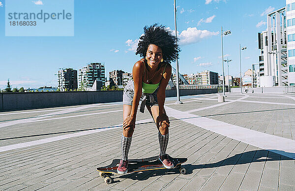Glückliche junge Frau  die auf einem Skateboard in der Stadt steht