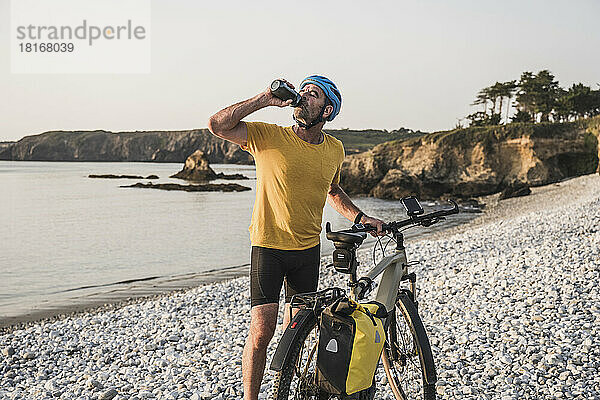 Reifer Mann mit Fahrrad-Trinkwasser am Strand