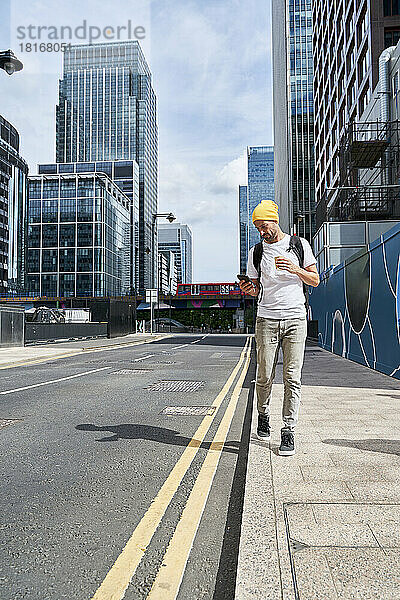 Mann benutzt Smartphone und geht an einem sonnigen Tag in der Stadt auf dem Fußweg spazieren
