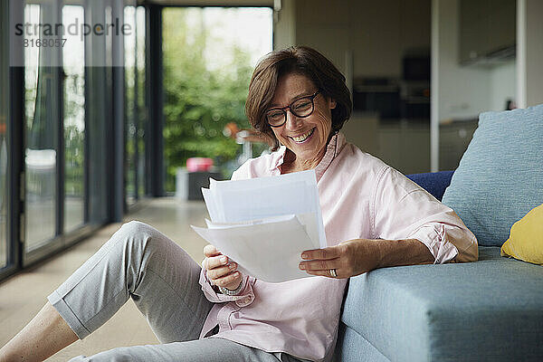 Glückliche Frau  die zu Hause auf dem Sofa sitzt und Dokumente liest