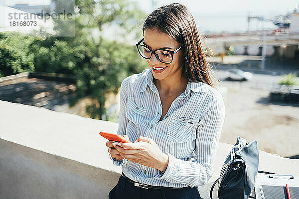 Glückliche Geschäftsfrau  die ihr Smartphone an der Wand lehnt