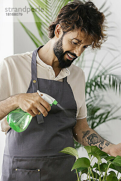 Lächelnder Mann sprüht Wasser auf Pflanze im Geschäft