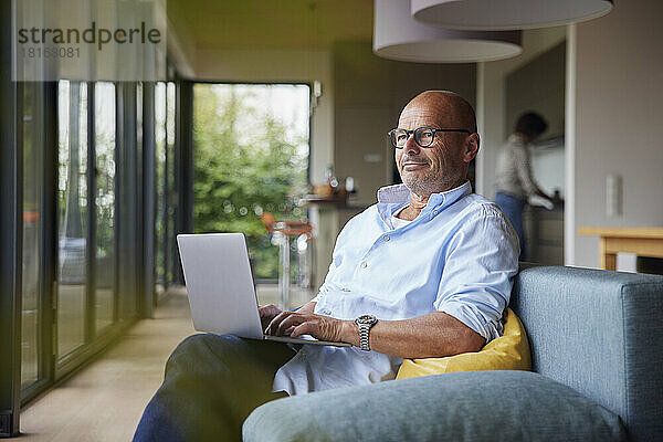 Nachdenklicher Mann mit Laptop sitzt zu Hause auf dem Sofa