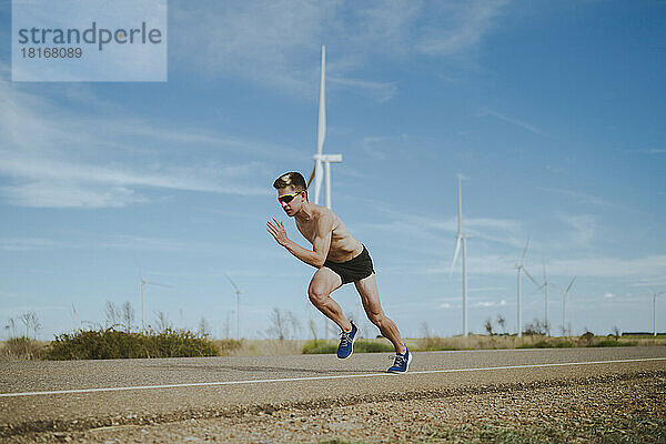 Entschlossener junger Athlet  der auf der Straße neben Windkraftanlagen läuft