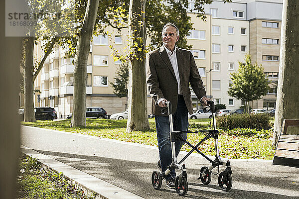 Lächelnder älterer Mann geht mit Gehhilfe auf Fußweg