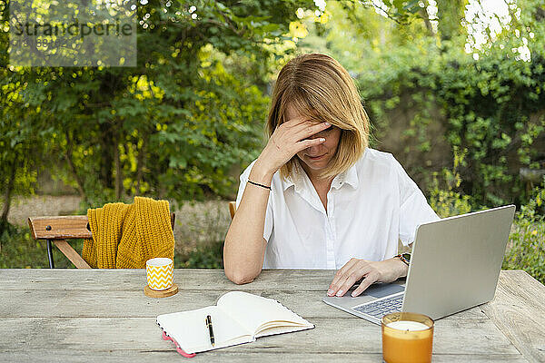 Gestresster Freiberufler sitzt mit Laptop am Tisch im Garten