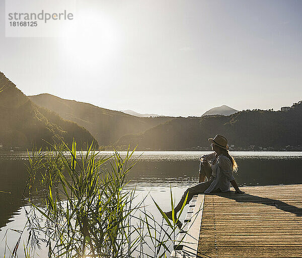 Frau entspannt sich auf Steg über See und Bergen