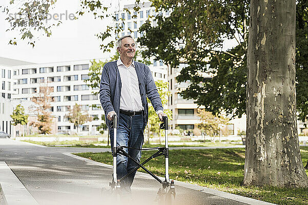 Lächelnder älterer Mann geht mit Gehhilfe auf Fußweg