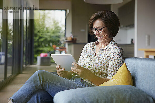 Glückliche Seniorin nutzt Tablet-PC auf dem heimischen Sofa