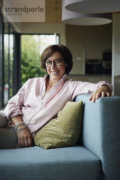 Happy woman wearing eyeglasses sitting on sofa at home