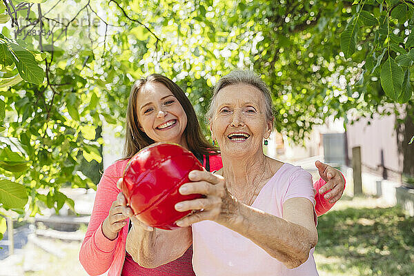 Fröhlicher Fitnesstrainer bringt Seniorin im Park Übungen mit Ball bei