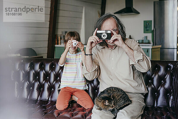 Großvater mit Vintage-Kamera und Enkelin mit Spielzeugkamera fotografieren zu Hause