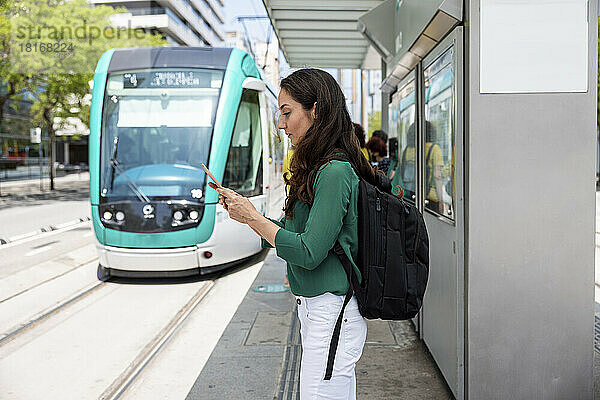 Frau benutzt Smartphone an Straßenbahnhaltestelle