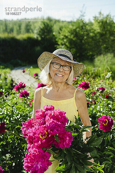 Glückliche Frau hält frische rosa Blumen im Garten