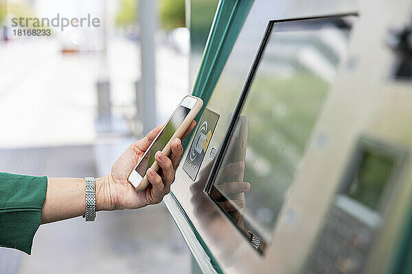 Hand einer Frau  die mit Smartphone am Fahrkartenautomaten scannt