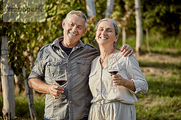 Glückliches älteres Paar hält Rotweingläser vor dem Weinberg