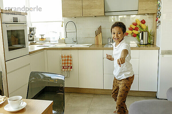 Happy boy gesturing fists standing in kitchen