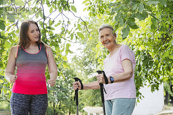 Fitnesstrainer unterrichtet ältere Frau mit Wanderstock im Park