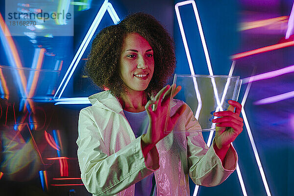Lächelnde junge Frau mit transparentem Laptop vor Neonlicht