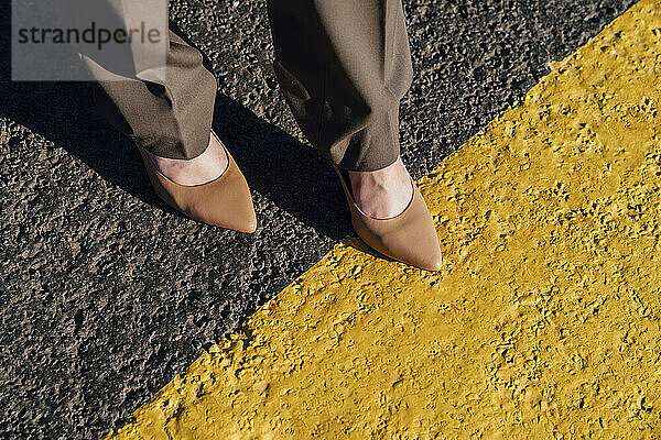 Businesswoman wearing brown stilettos over yellow line marking on road