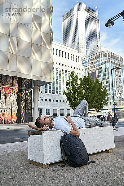 Mann entspannt sich auf Bank vor Gebäuden