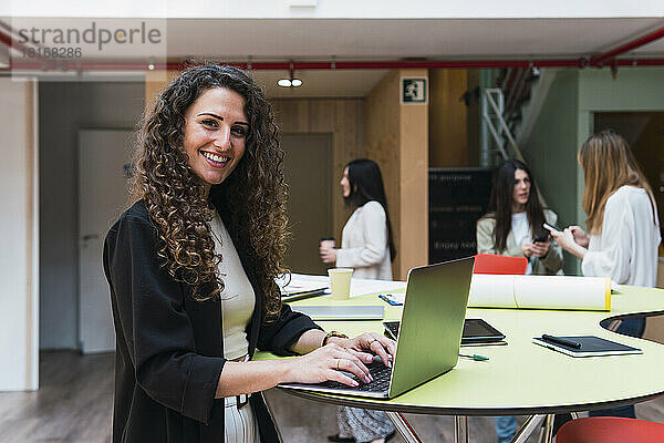 Porträt einer lächelnden brünetten Geschäftsfrau  die im Büro einen Laptop benutzt