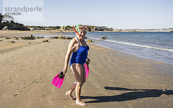 Glückliche Frau mit Taucherflossen beim Spaziergang am Strand
