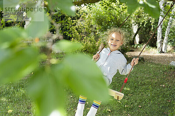 Lächelndes Mädchen schaukelt im Garten