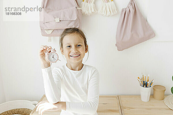 Happy girl showing pink alarm clock at home