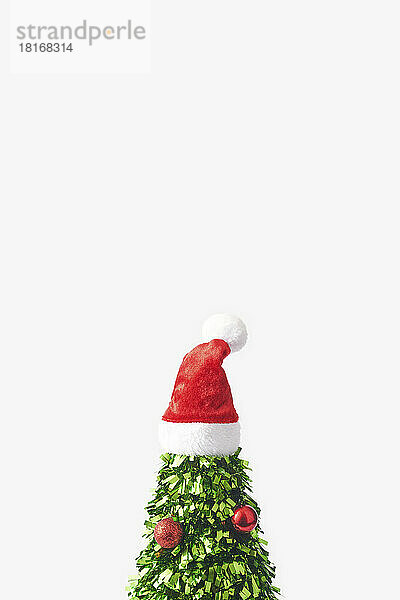 Weihnachtsbaum aus grünem Konfetti mit Weihnachtsmütze an der Spitze vor weißem Hintergrund