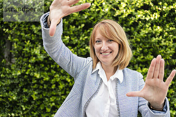 Reife Frau macht Fingerrahmen vor Hecke im Garten