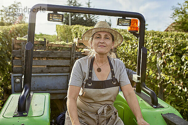 Reifer Bauer mit Strohhut auf Traktor im Weinberg