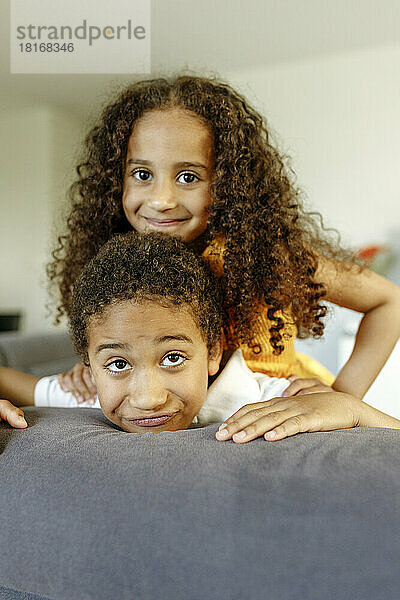 Smiling girl with curly hair leaning on brother at home