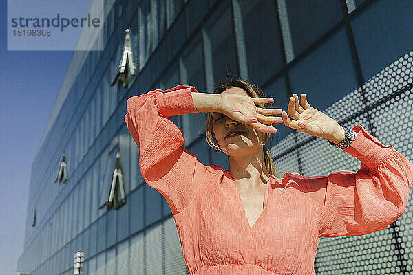 Frau bedeckt Augen mit Händen vor Gebäude