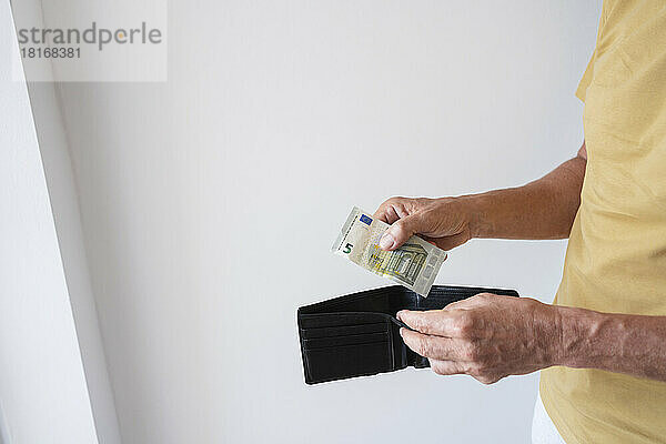 Hände eines Mannes mit Geldbörse und Geldschein  der zu Hause an der Wand steht