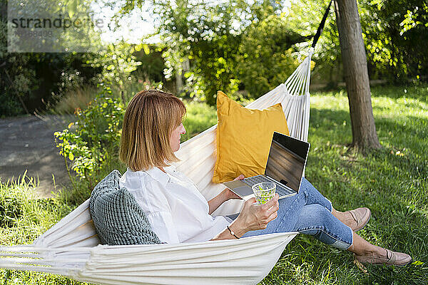 Freiberufler sitzt mit Laptop in der Hängematte im Garten