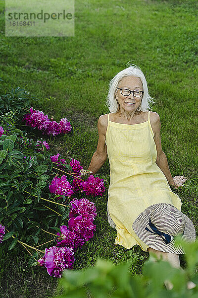Lächelnde Frau entspannt sich neben Blumen im Garten