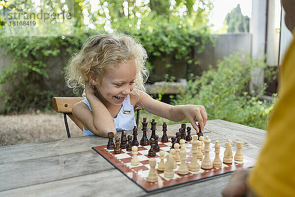 Glückliches blondes Mädchen  das Schach im Garten spielt